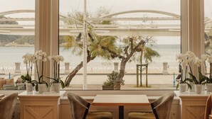 Een eetgedeelte met uitzicht op zee en een brug, met een tafel, stoelen, potplanten en een vloer met patroon.