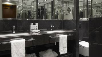 A modern bathroom with a large mirror, two sinks, and a toilet.