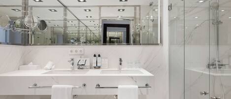 A modern bathroom with a large mirror, two sinks, a shower, and a glass-enclosed shower area.