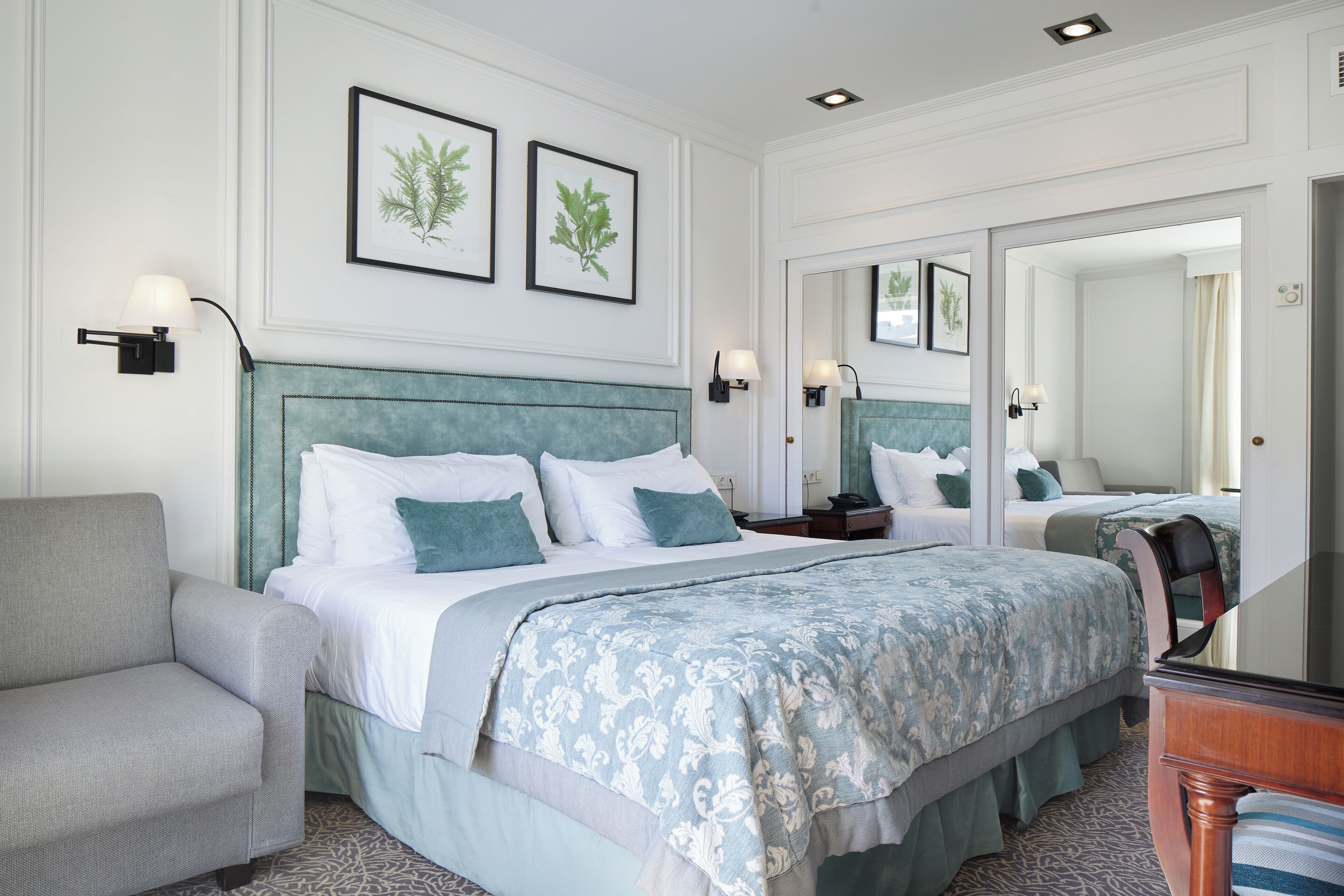 A hotel room with a large bed, a sofa, a nightstand, and a mirror.