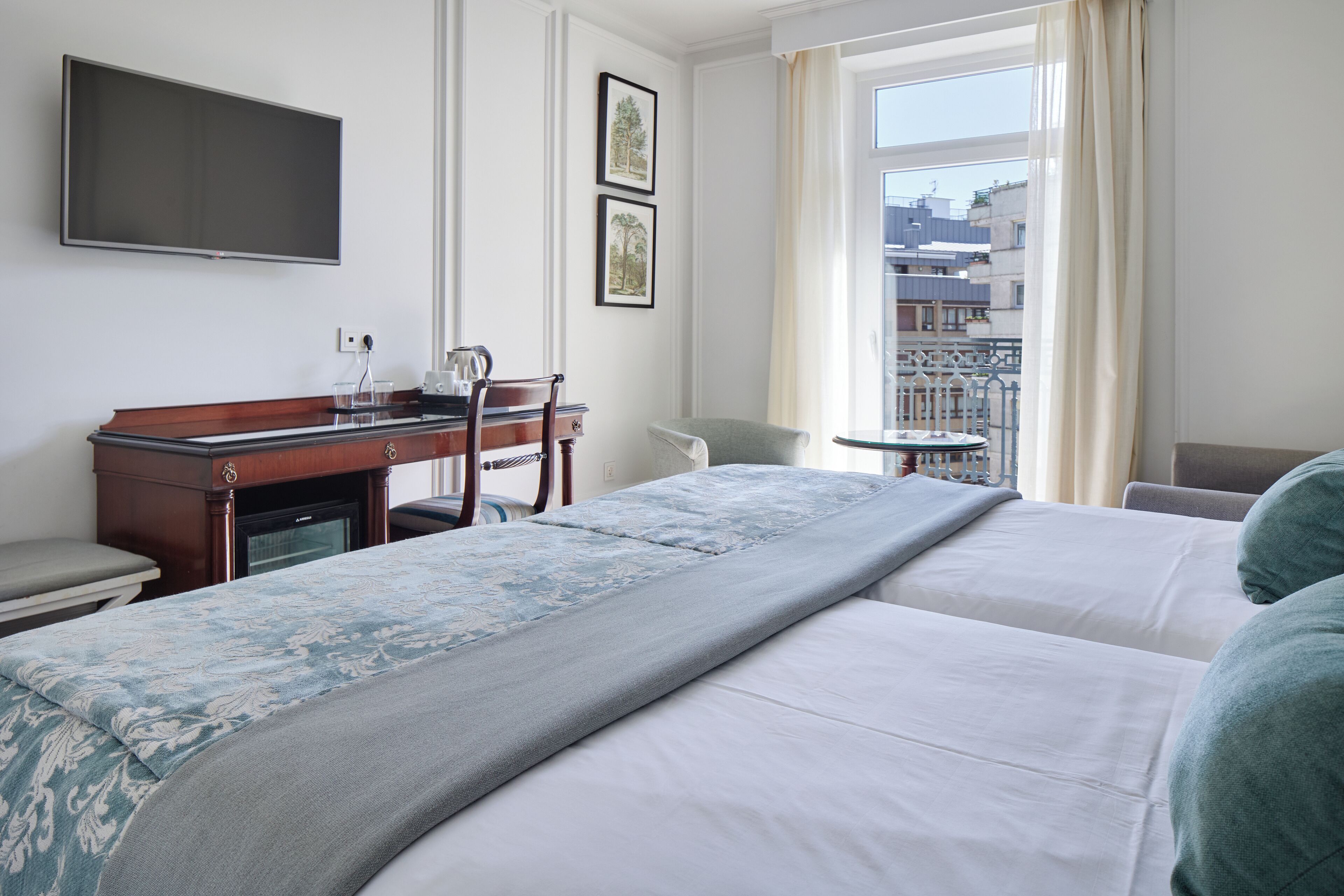 Une chambre d’hôtel avec deux lits, un bureau avec une chaise, une télévision et une fenêtre donnant sur des immeubles.