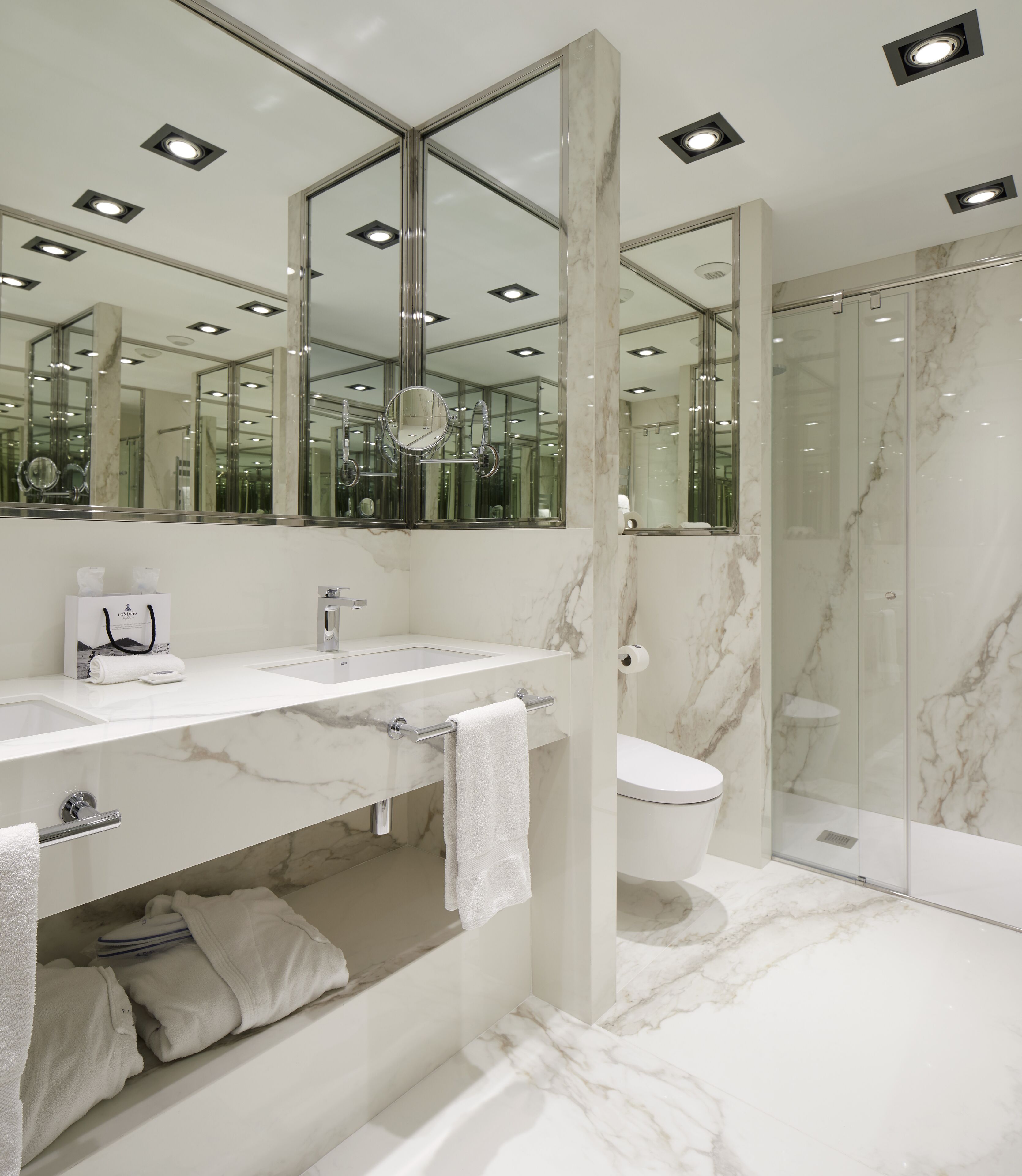 A modern bathroom with a marble sink, a large mirror, and a glass shower enclosure.
