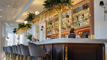 Una zona de bar con una barra larga, taburetes y un techo decorado con candelabros.