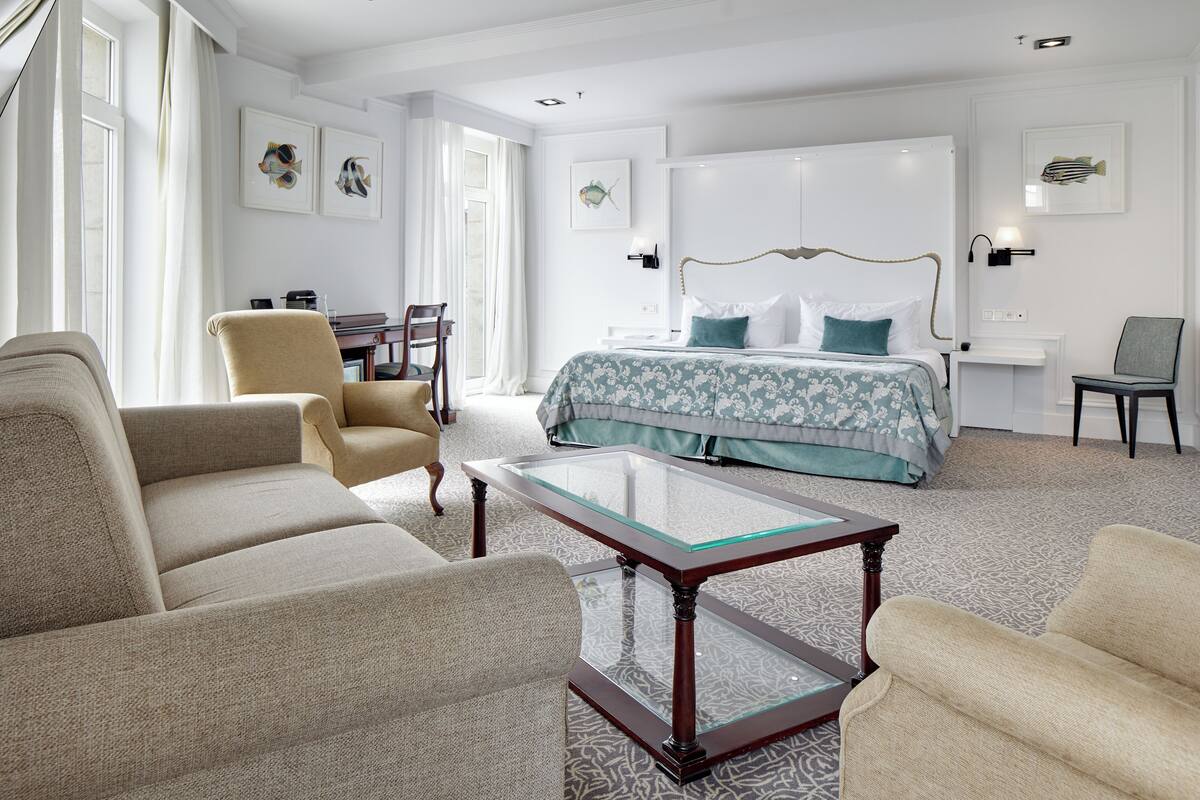 Een hotelkamer met een bed, twee fauteuils, een glazen salontafel en kunstwerken aan de muren.