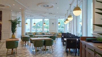 A restaurant with a geometric patterned floor, green upholstered chairs, and pendant lighting.