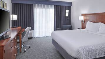 Een hotelkamer met een groot bed, een bureau met stoel, een televisie en een raam met gordijnen.