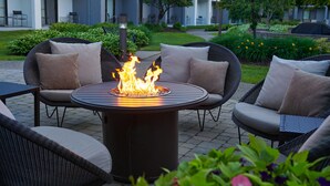 A circular outdoor seating area with a fire feature, surrounded by wicker chairs with cushions. - Courtyard by Marriott Detroit Troy (Troy)