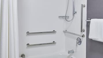 A modern bathroom with a white bathtub, grab bars, a showerhead, and a towel rack.