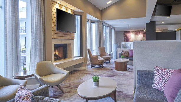 A modern living room with a fireplace, comfortable seating, and large windows. - Courtyard by Marriott Detroit Troy (Troy)