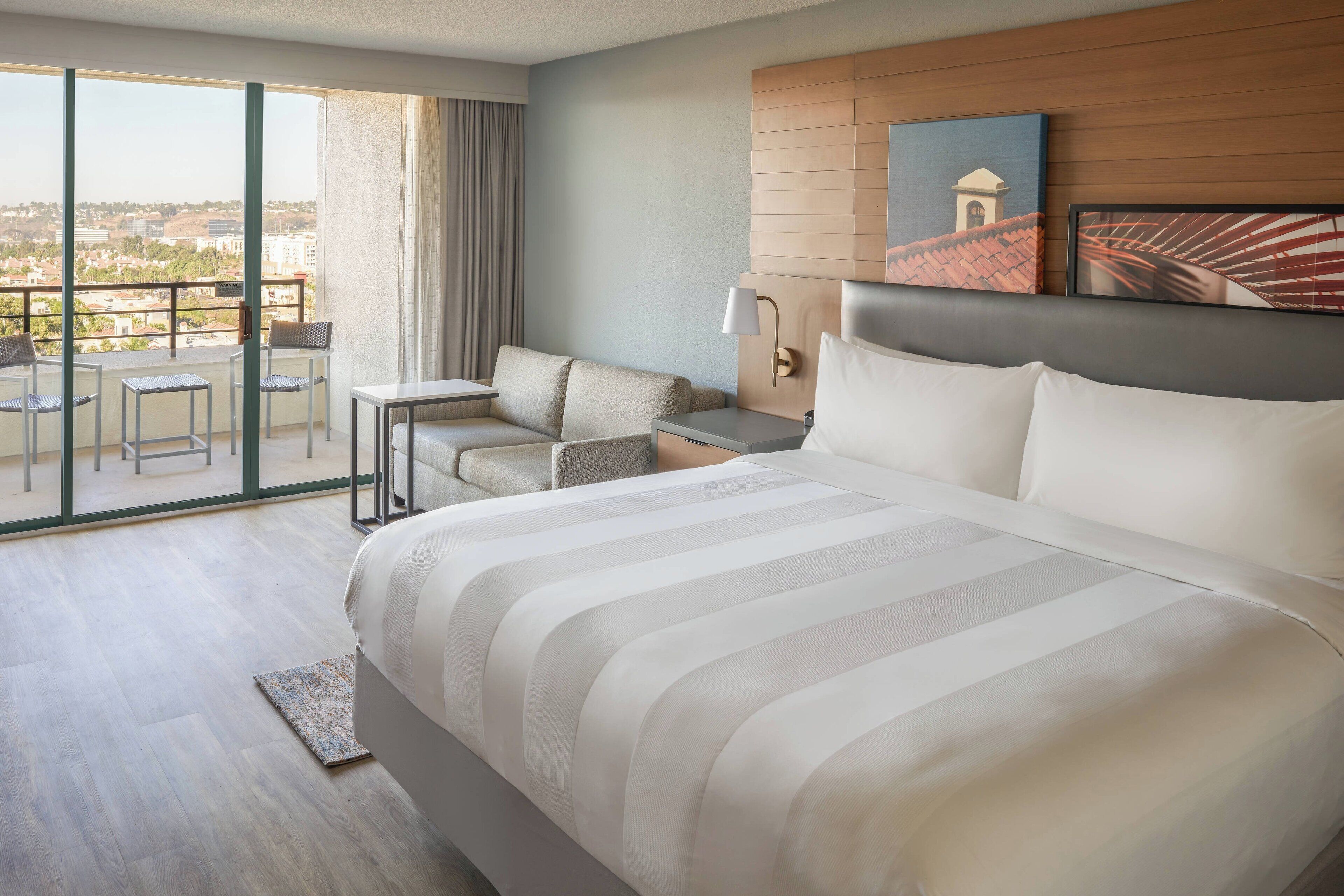 Hotelkamer met een groot bed, een bureau, een stoel en een balkon met uitzicht op de stad.