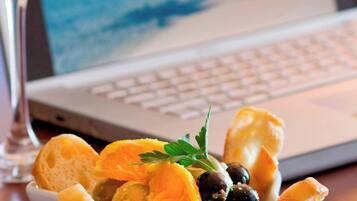 Una computadora portátil con un fondo de pantalla de playa, una copa de vino blanco y un cuenco con aceitunas y pan sobre una mesa.