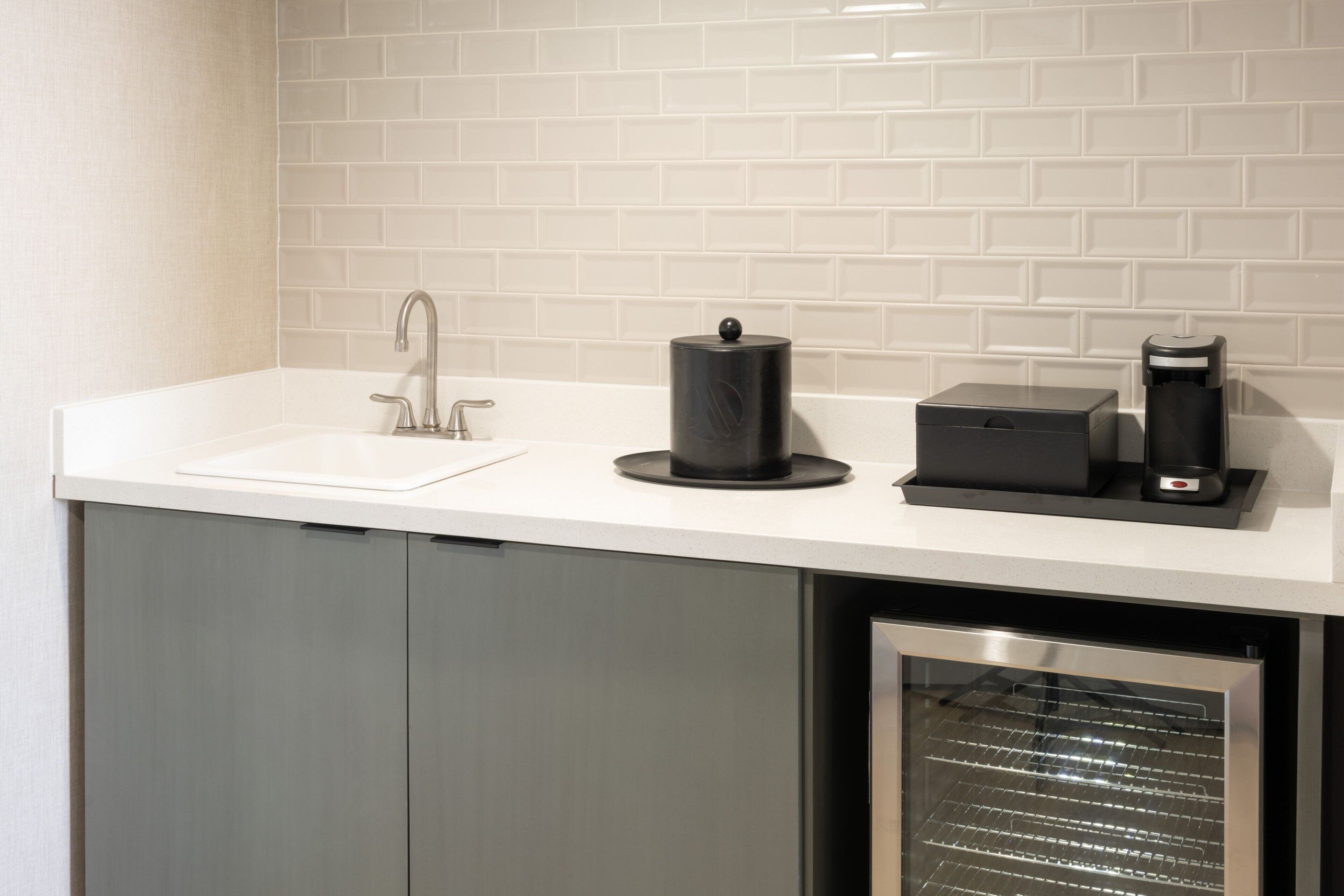 A modern kitchen with a white countertop, a stainless steel sink, a coffee machine, and a built-in oven.