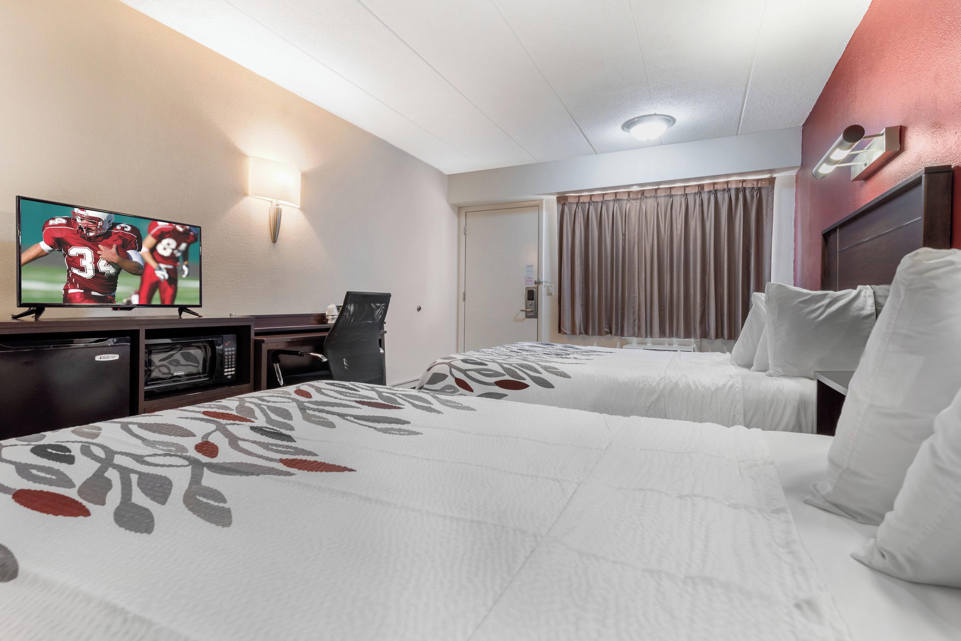 Une chambre d’hôtel avec deux lits, une télévision, un bureau avec un ordinateur et un four à micro-ondes.