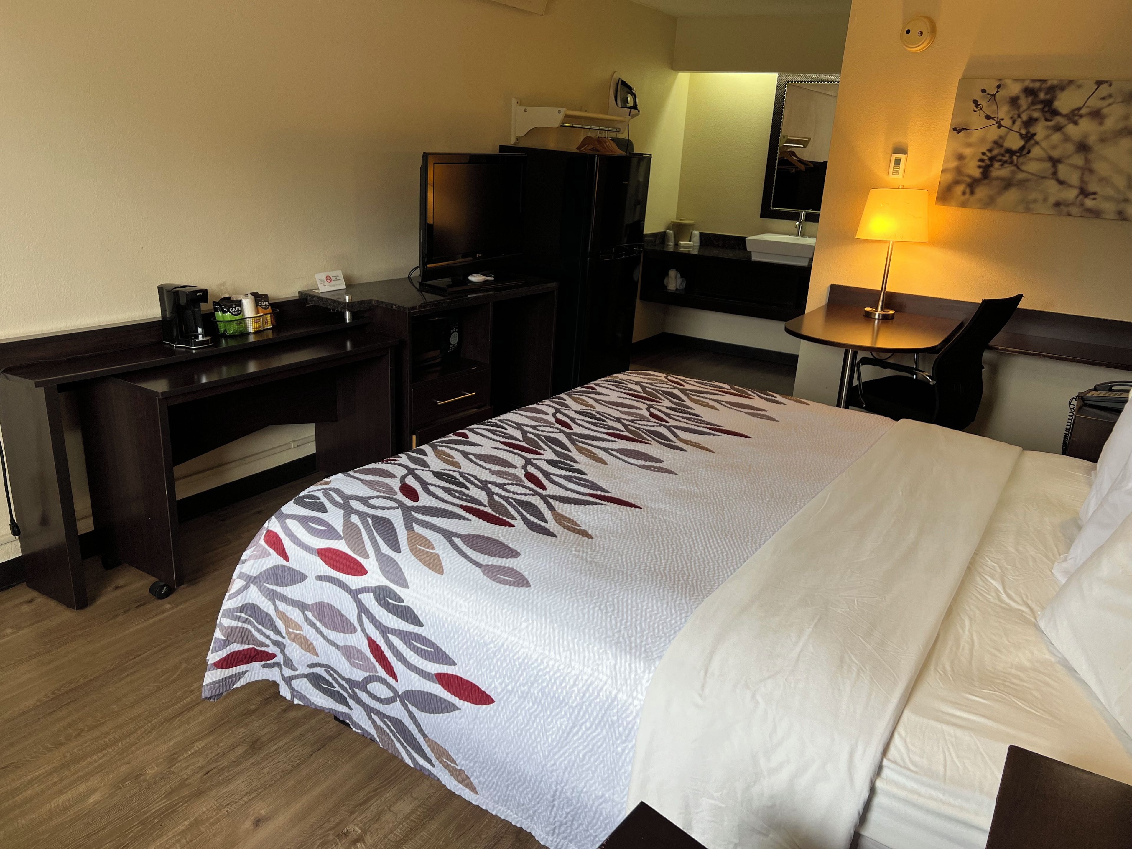 A hotel room with a bed, desk, and a small table with a lamp.