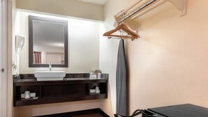 A bathroom with a sink, mirror, towel rack, and a black suitcase. - Red Roof Inn Lafayette - Purdue University (Lafayette)