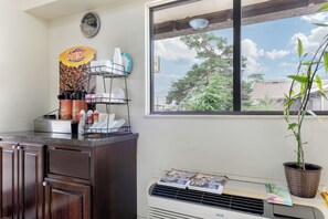 A kitchen with a window, a clock, and a newspaper rack. - Red Roof Inn Lafayette - Purdue University (Lafayette)