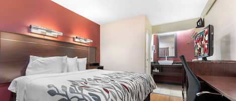 A hotel room with a bed, a desk, a chair, a mirror, and a television.