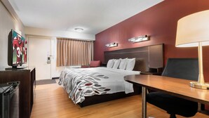 A hotel room with a bed, desk, chair, television, and a red accent wall. - Red Roof Inn Lafayette - Purdue University (Lafayette)