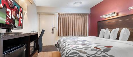 Habitación de hotel con cama, escritorio con televisor, silla, puerta y ventana con cortinas.