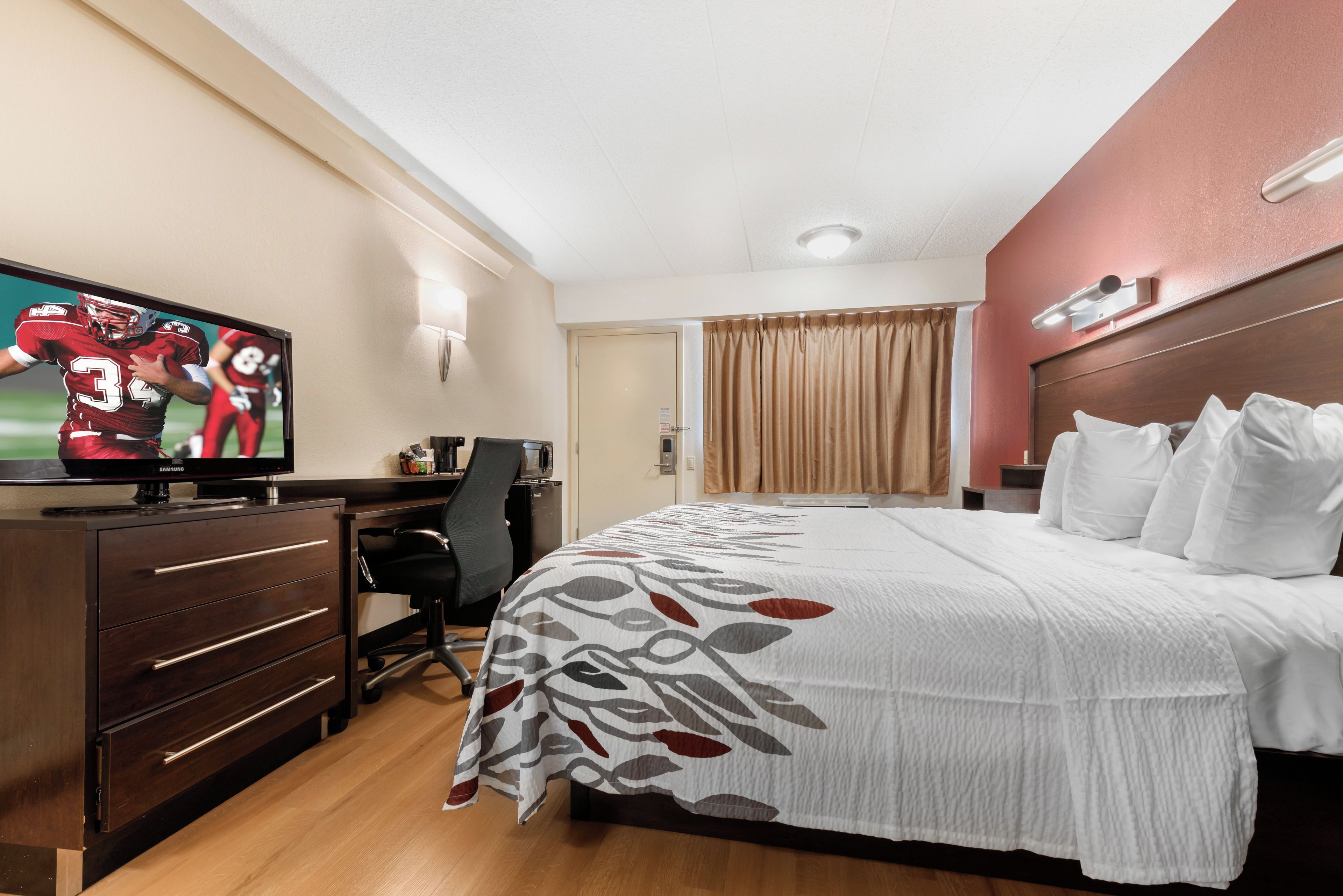 A hotel room with a bed, a desk, a television, and a window with curtains.