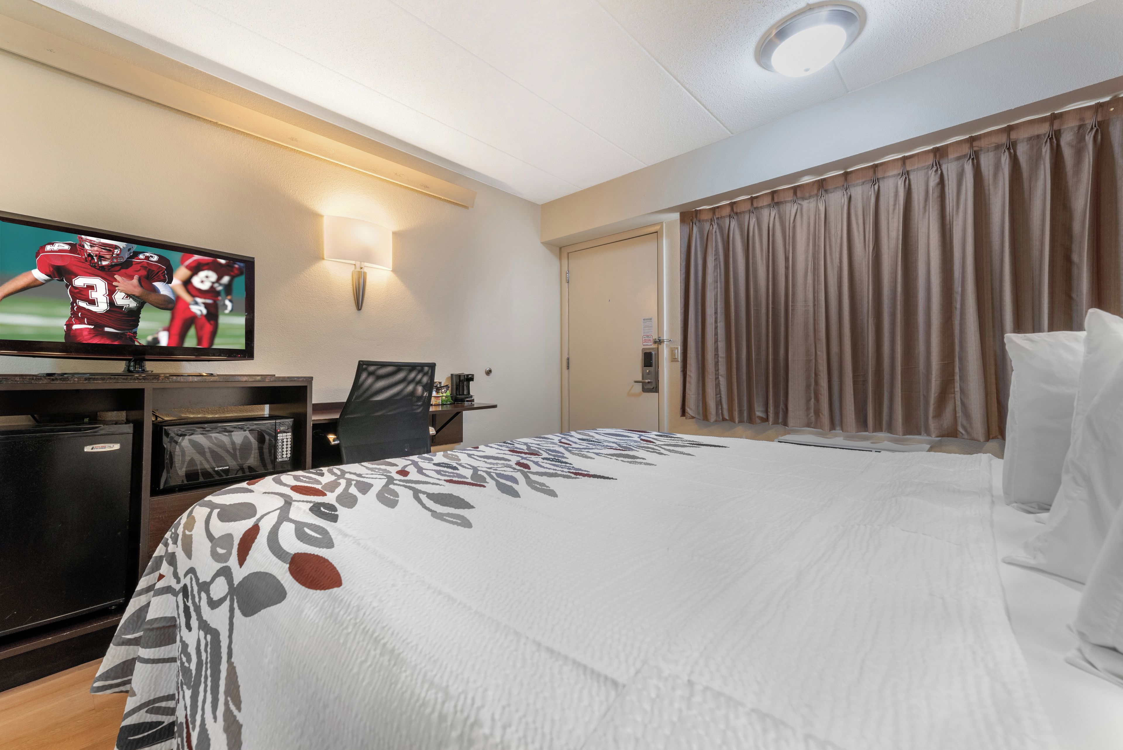 A hotel room with a bed, a desk, a television, and a door.