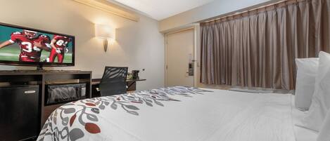 A hotel room with a bed, a desk, a television, and a door.