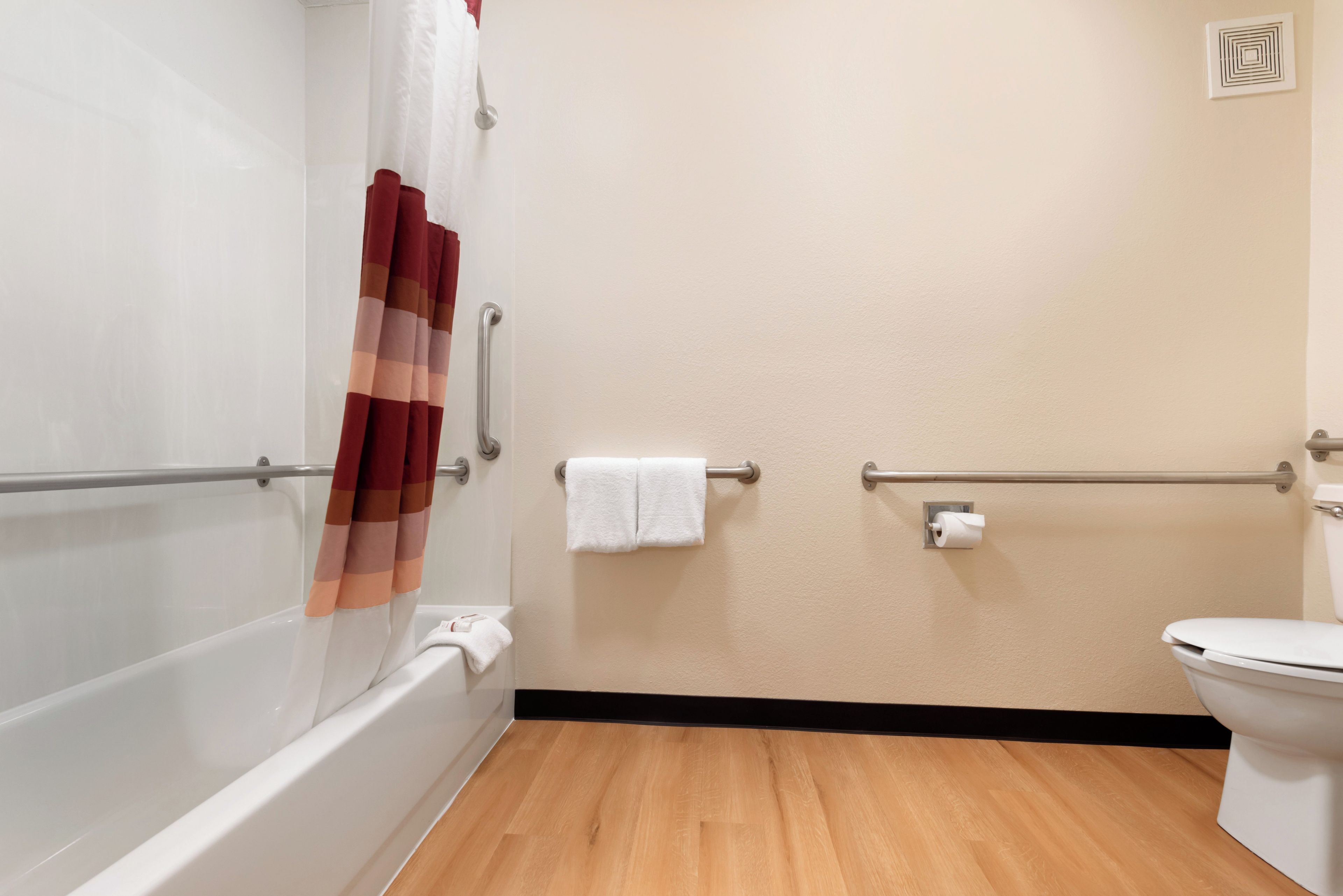 A bathroom with a bathtub, toilet, and handrails.