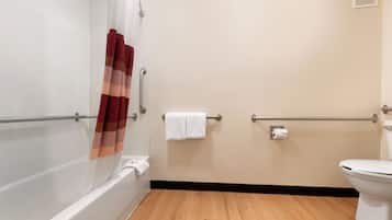 A bathroom with a bathtub, toilet, and handrails.