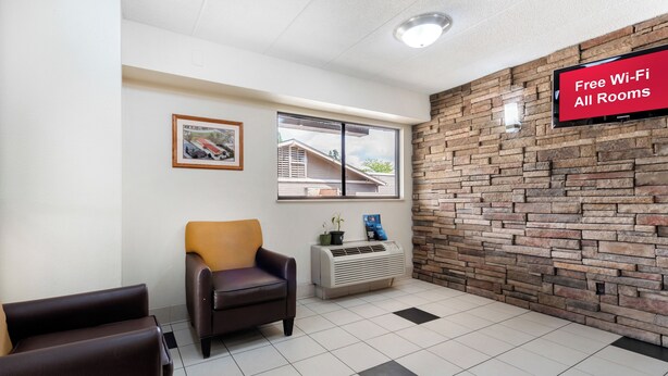A room with a stone wall, a window, a framed picture, a chair, and a sign indicating free Wi-Fi availability. - Red Roof Inn Lafayette - Purdue University (Lafayette)