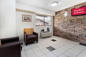 A room with a stone wall, a window, a framed picture, a chair, and a sign indicating free Wi-Fi availability. - Red Roof Inn Lafayette - Purdue University (Lafayette)