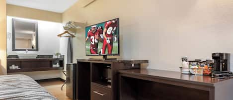 Quarto de hotel com cama, escrivaninha, televisão de tela plana, espelho, minibar e máquina de café.