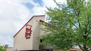 A Red Roof Inn with a stone facade, a stone bench, and a tree in front. - Red Roof Inn Lafayette - Purdue University (Lafayette)