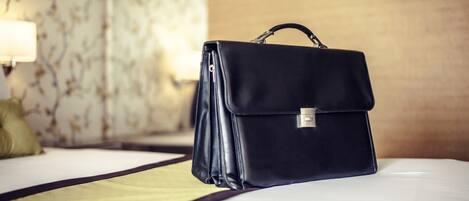 A black briefcase on a bed with a patterned wallpaper background.