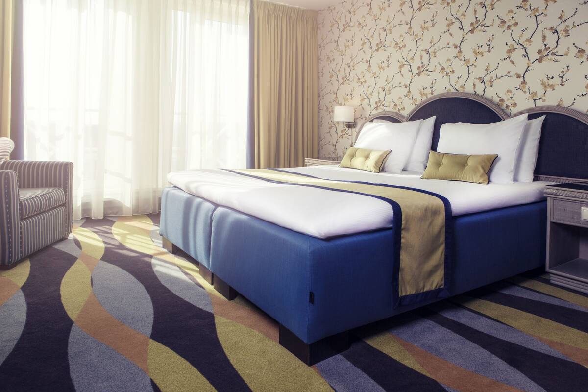 A hotel room with a large bed, a chair, a nightstand, and a lamp.