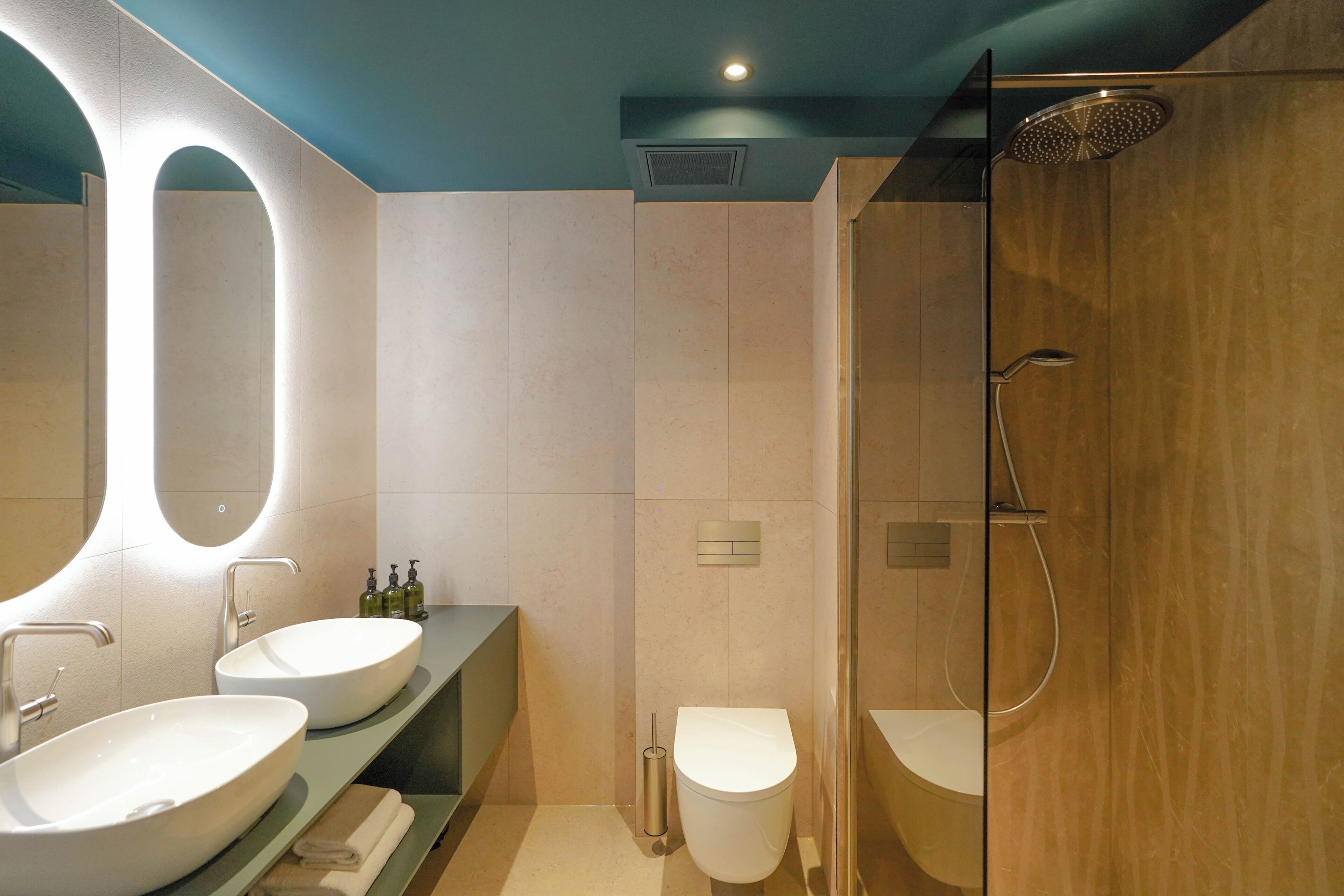 A modern bathroom with two sinks, a toilet, and a shower.
