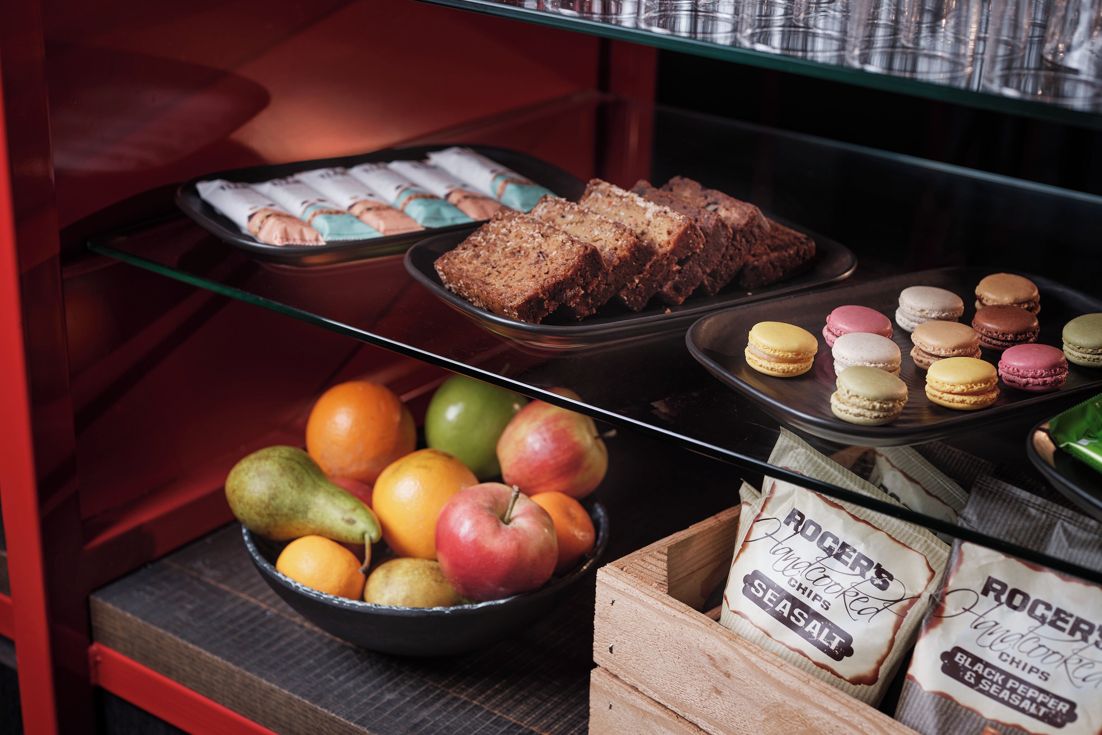 A bakery display with pastries, macarons, and a bowl of fruits.
