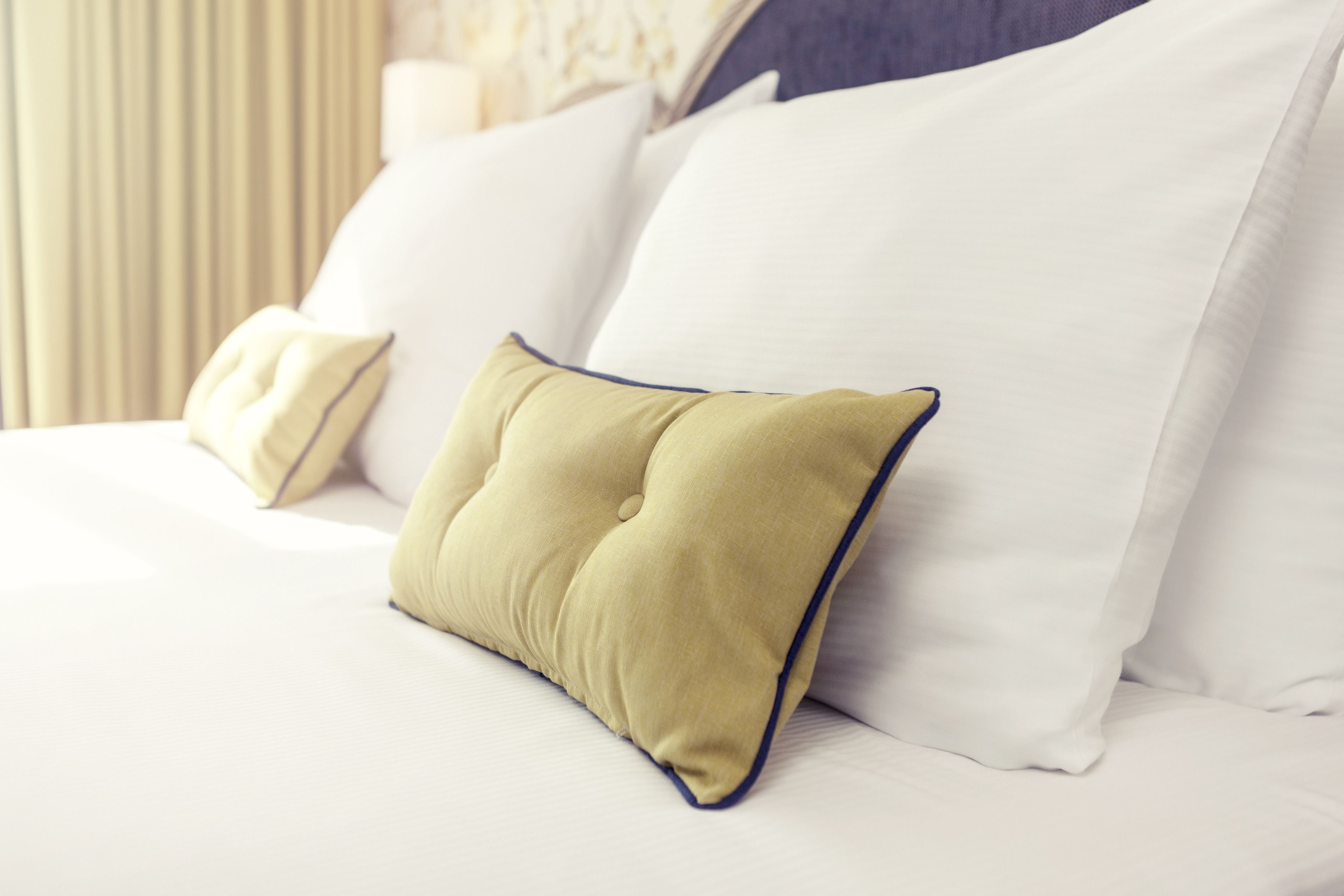 Una cama bien tendida con sábanas blancas y una única almohada verde con ribete azul.