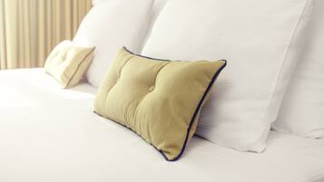 Una cama bien tendida con sábanas blancas y una única almohada verde con ribete azul.