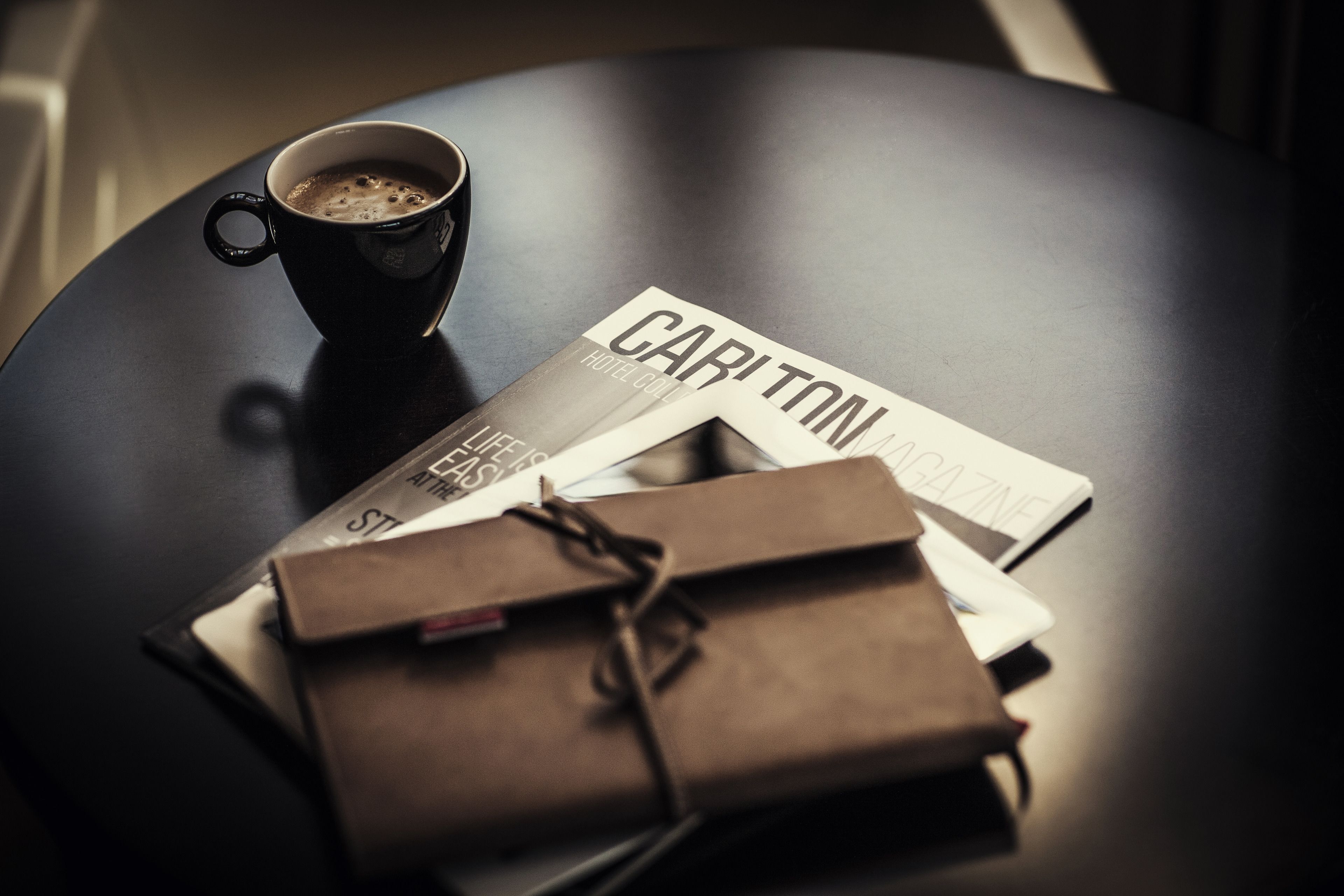 Ein schwarzer Tisch mit einer Kaffeetasse, einer Zeitschrift und einem braunen Paket.