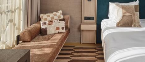 Una habitación de hotel con sofá cama, mesita de noche, escritorio pequeño y cama con almohadas.