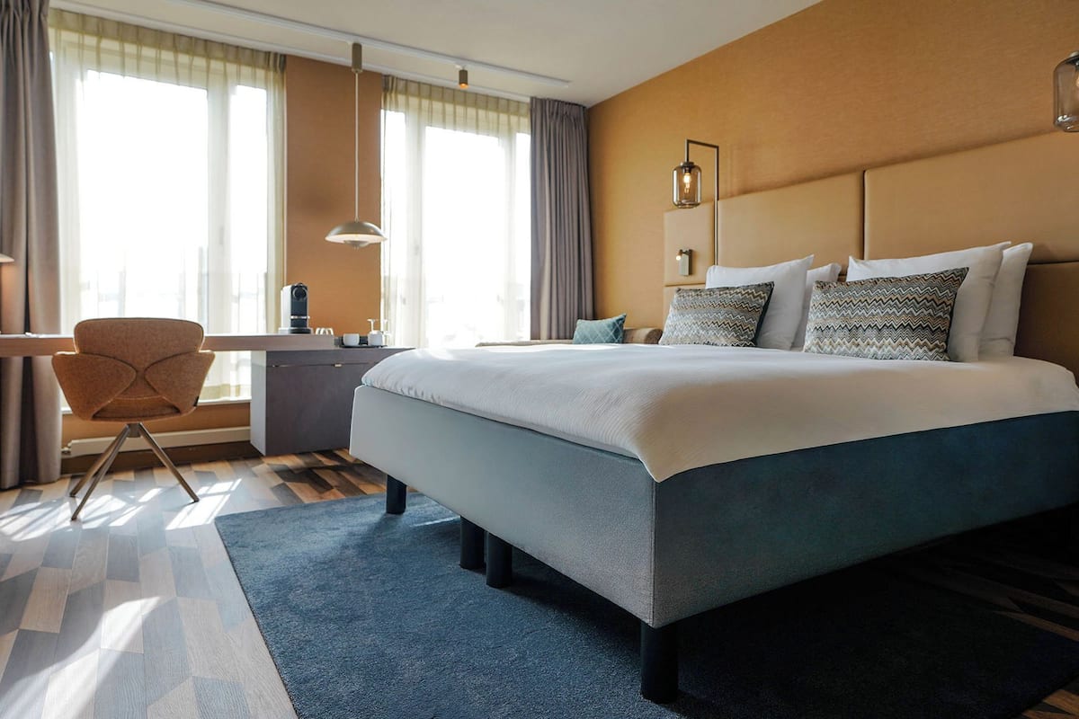 A modern hotel room with a large bed, a desk, and a chair.