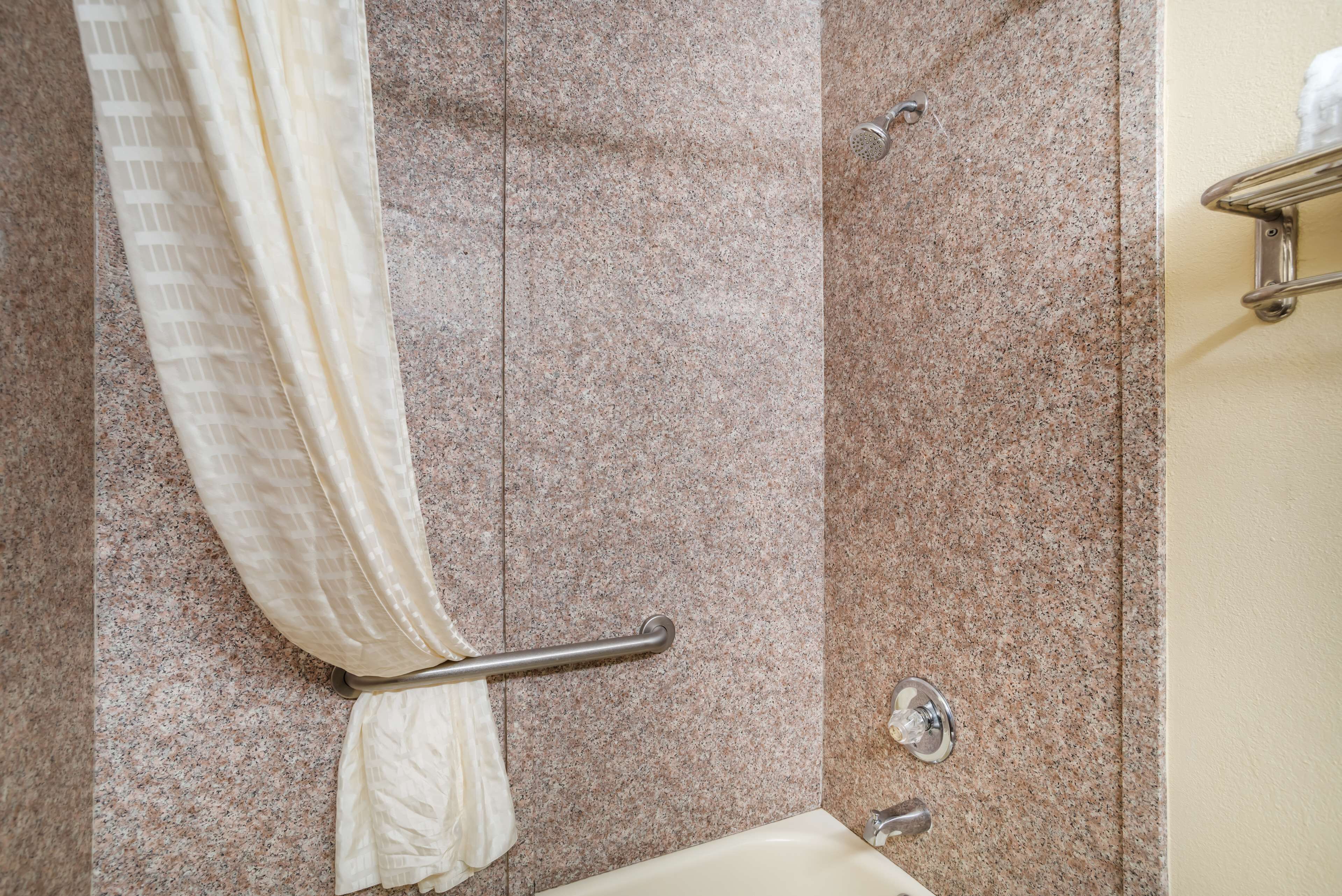 A bathroom with a granite countertop, a shower with a handheld showerhead, and a towel rack.