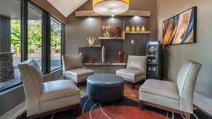 A modern lounge area with leather chairs, a round ottoman, a large pendant light, and a fireplace with decorative items. - Best Western Charlotte-Gastonia (Gastonia)