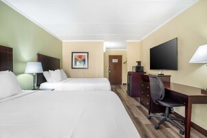 Una habitación de hotel con dos camas, un escritorio, una silla, un televisor y una lámpara de escritorio.