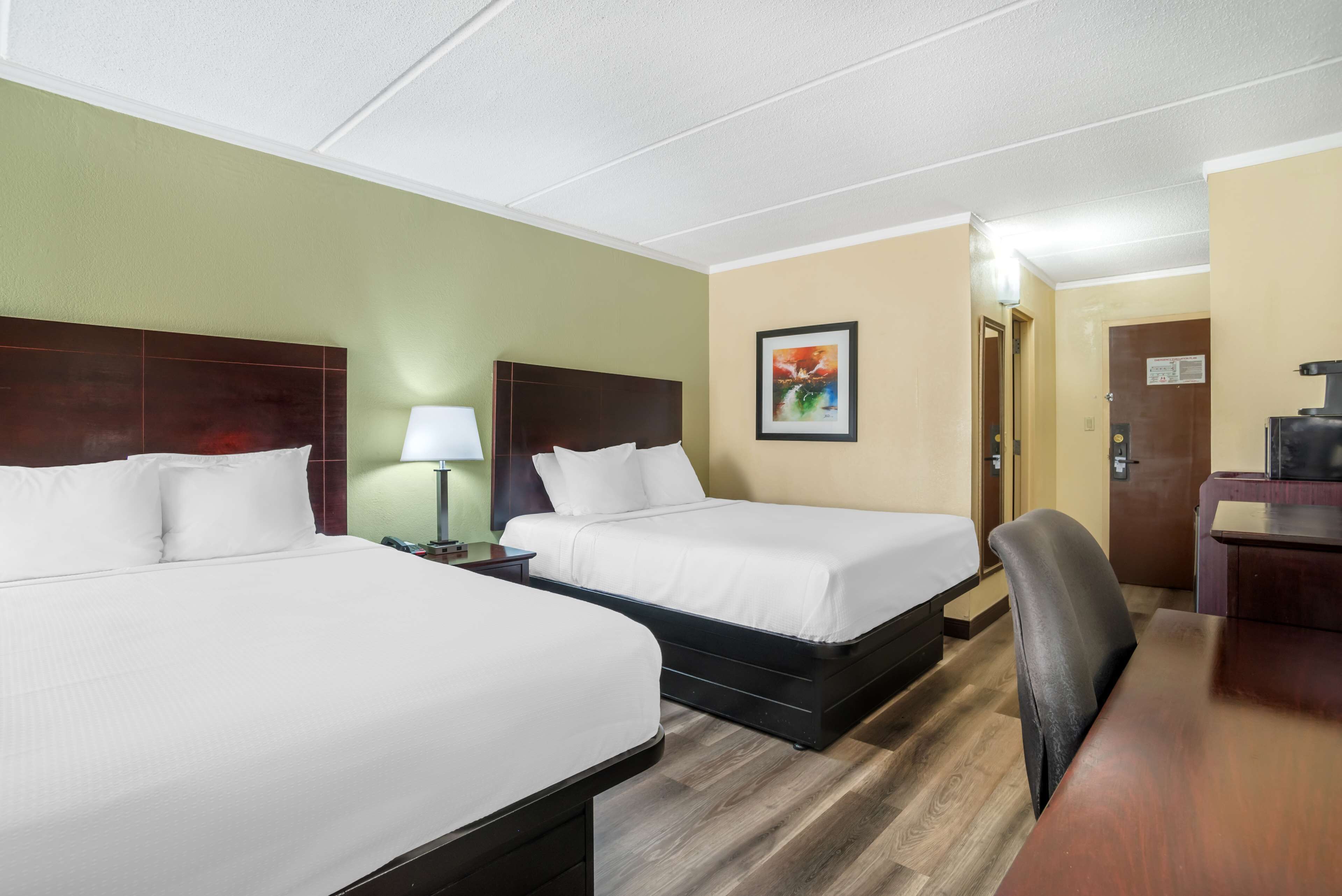A hotel room with two beds, a desk, a chair, and a painting on the wall.