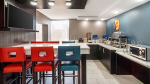 A modern kitchen with a flat-screen TV, red and blue chairs, a microwave, and a coffee machine. - Best Western Charlotte-Gastonia (Gastonia)