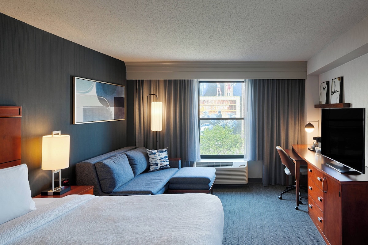 A hotel room with a bed, a sofa, a desk, a television, and a window with curtains.