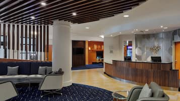 A modern hotel lobby with a reception desk, seating area, and a check-in counter.