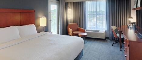 A hotel room with a large bed, a desk, a chair, and a view of the outdoors.