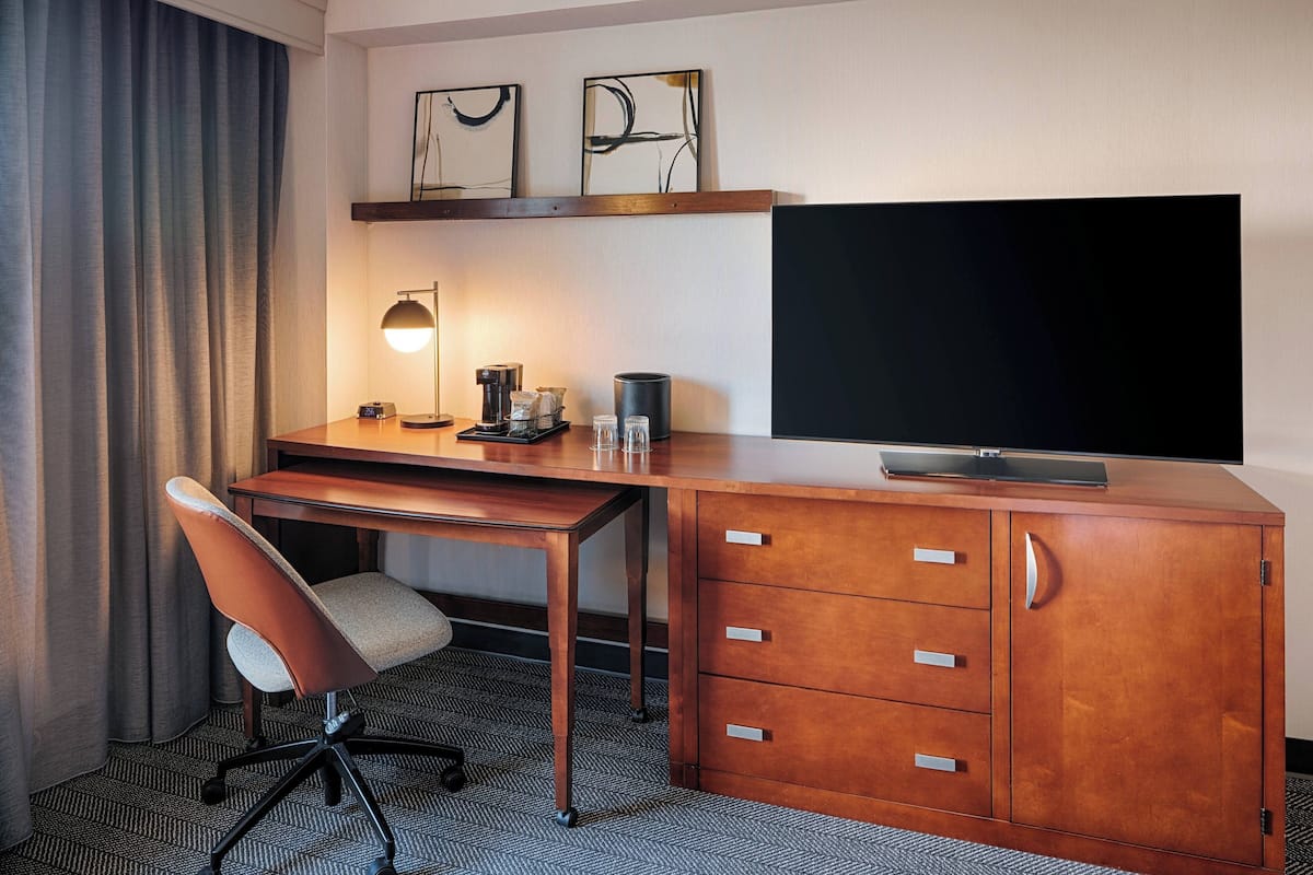 A hotel room with a wooden desk, a chair, a television, and a cabinet with drawers.